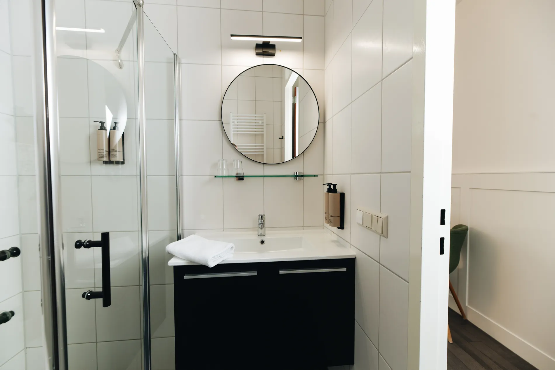 Overzicht van een frisse badkamer in Resort Land & Zee, uitgerust met hoogwaardig sanitair, witte tegels en luxe wanddispensers voor zeep.